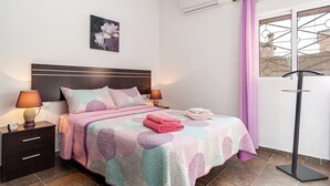 Een slaapkamer met een bed, nachtkastjes, een wandairconditioner, een raam met gordijn en een vloerlamp.