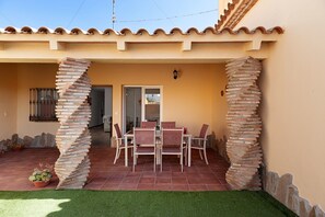 Zona de pati amb taula i cadires, una porta i una paret amb un pilaret decoratiu.