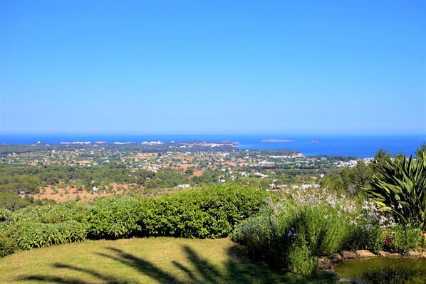 Una vista panorámica de un pueblo costero con cielo despejado, abundante vegetación y una masa de agua distante.