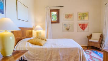 Un dormitorio con una cama, dos lámparas de noche, un sillón de mimbre y decoración en la pared.