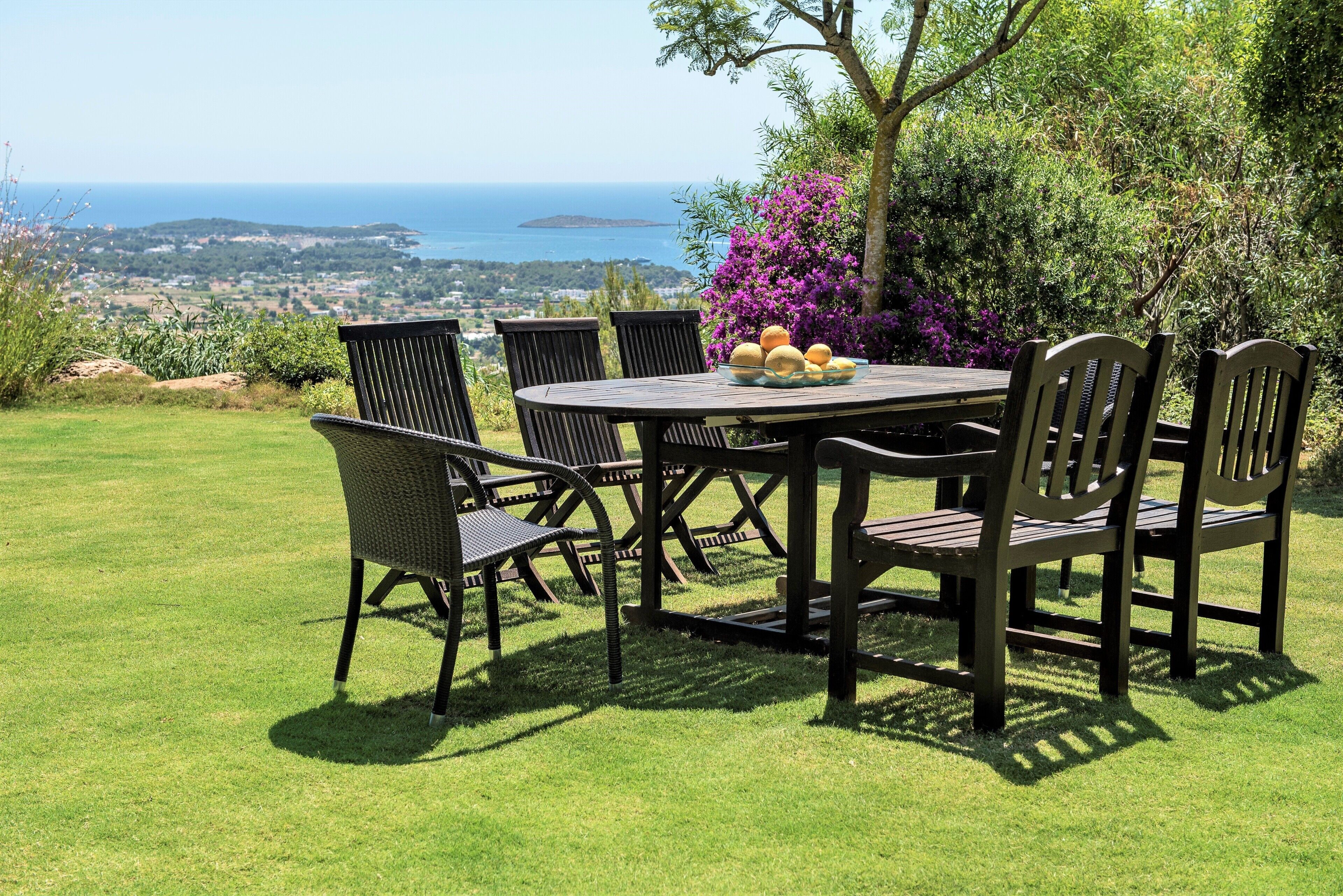 A dining table with chairs, a view of the sea, and a grassy area.