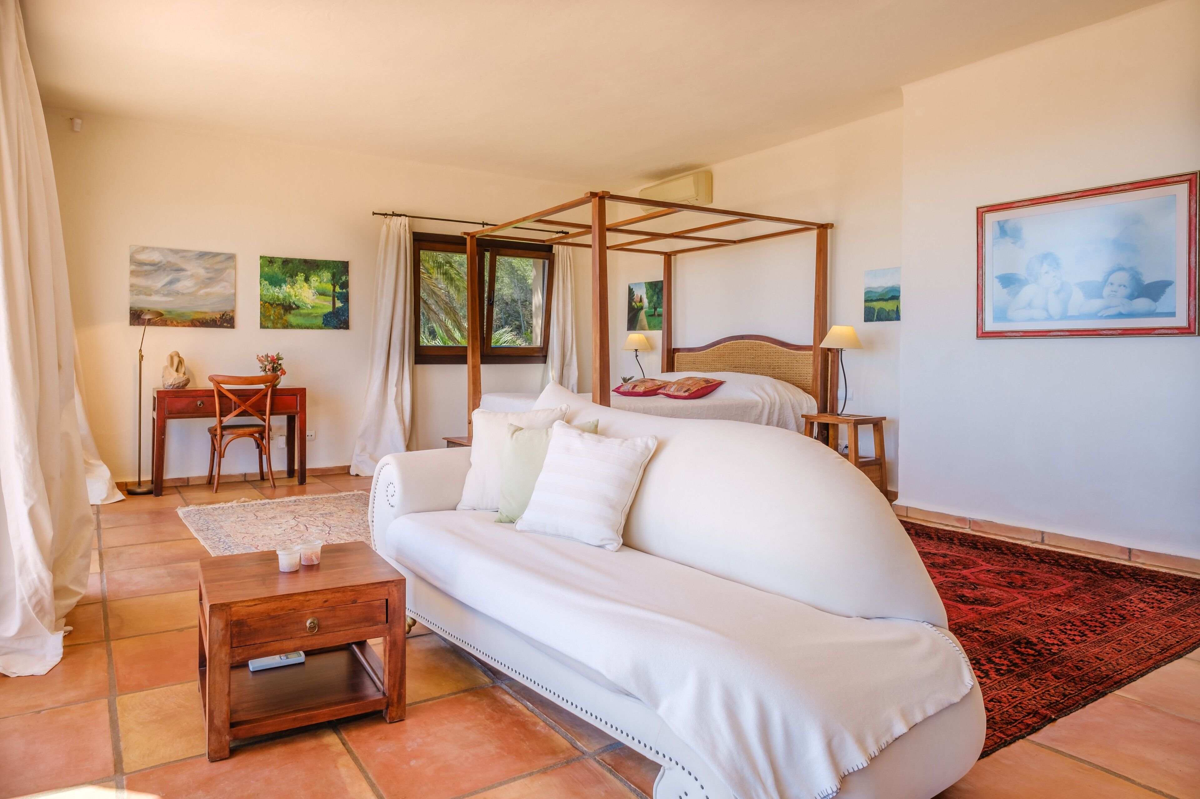 Une chambre à coucher avec un lit à baldaquin, un canapé blanc, une table de chevet en bois et un tapis rouge à motifs.