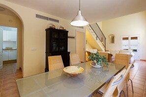 Een eetgedeelte met een glazen tafel, rieten stoelen, een hanglamp en een trap op de achtergrond.