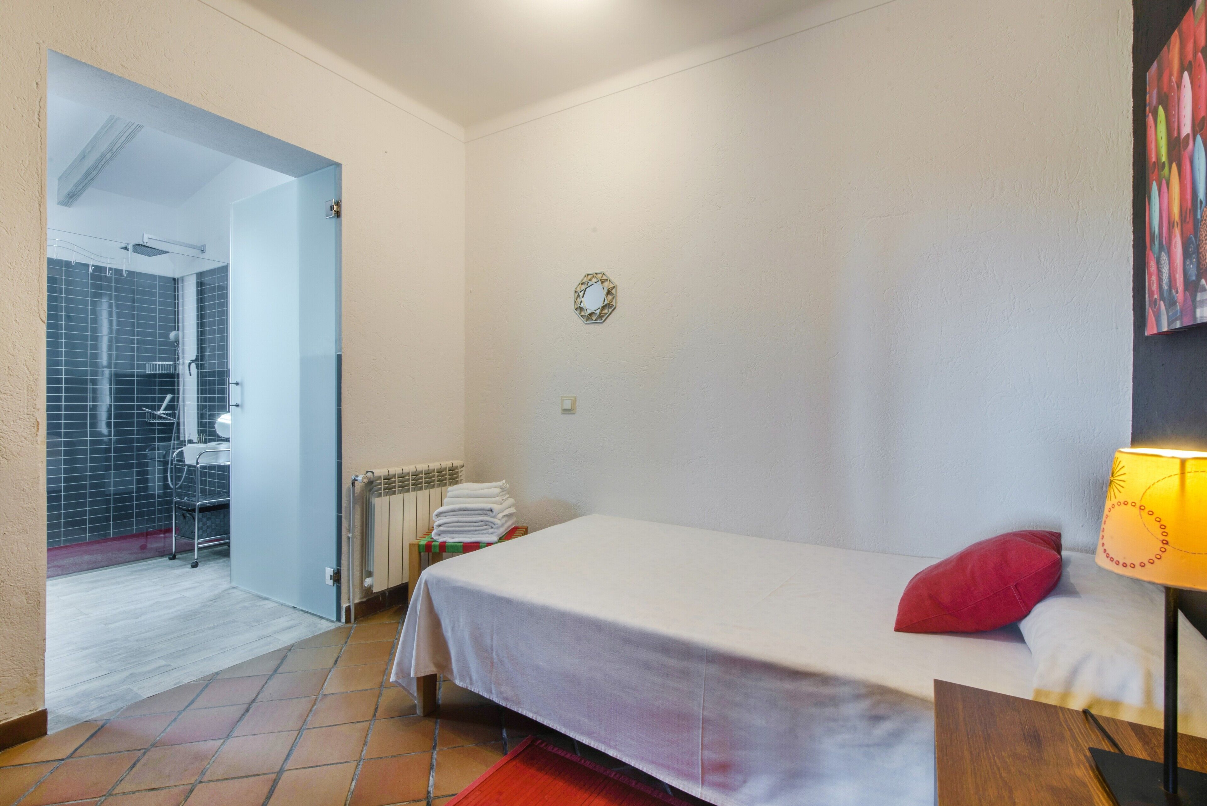 Une chambre à coucher avec un lit, un oreiller rouge, une lampe, un radiateur et une porte donnant sur une salle de bain.