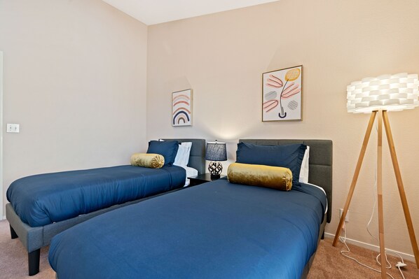 A bedroom with two single beds, a bedside table with a lamp, and a floor lamp.