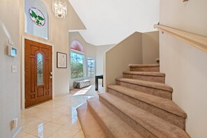 A spacious hallway with a wooden door, a staircase, and a bench.