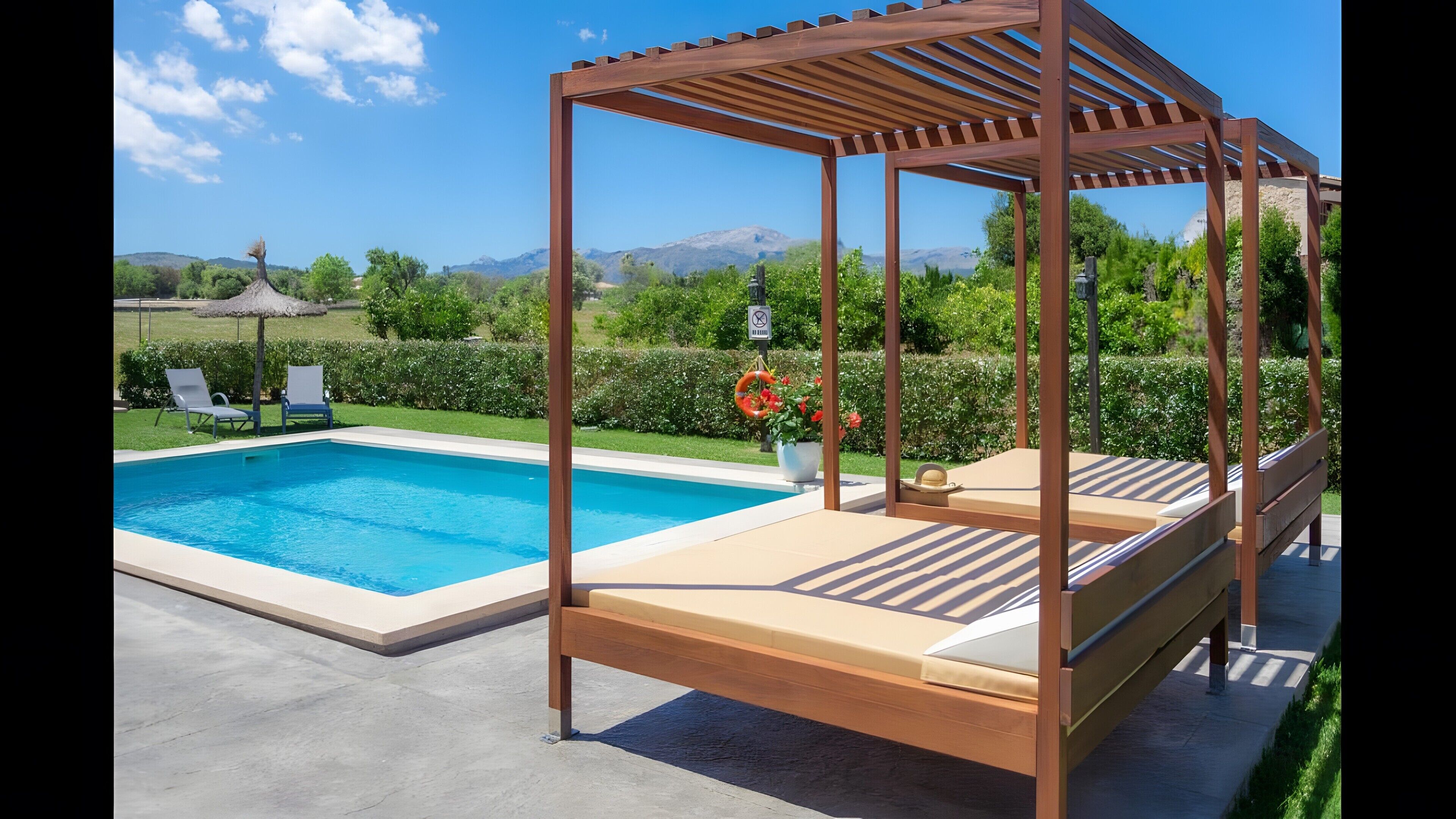 Ein Pool mit einer Holzpergola und Liegestühlen, umgeben von viel Grün und Bergen im Hintergrund.