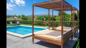 A pool with a wooden pergola and lounge chairs, surrounded by greenery and mountains in the background. - Rural Charm with Pool – Villa Damián 12 (Alcúdia)