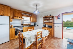 Una cocina con armarios de madera, una mesa de comedor y vista a una piscina.