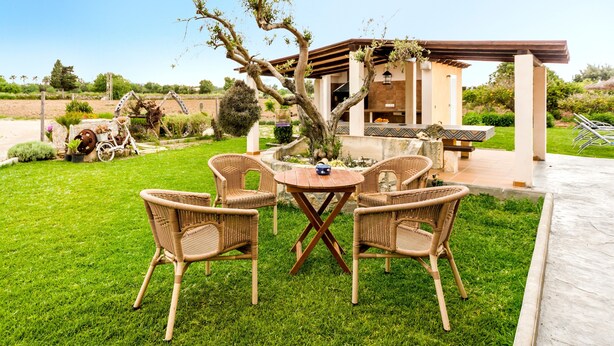 A patio with wicker chairs and a table, a small building with a pergola, and a tree in the foreground. - Rural Charm with Pool – Villa Damián 12 (Alcúdia)
