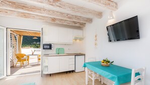 A compact kitchen with white cabinets, a microwave, and a green toaster. There's a dining area with a turquoise tablecloth and a basket of fruit. - Apartment Close to the Beach with Pool Access, Private Terrace, Air Conditioning and Wi-Fi (Canyamel)