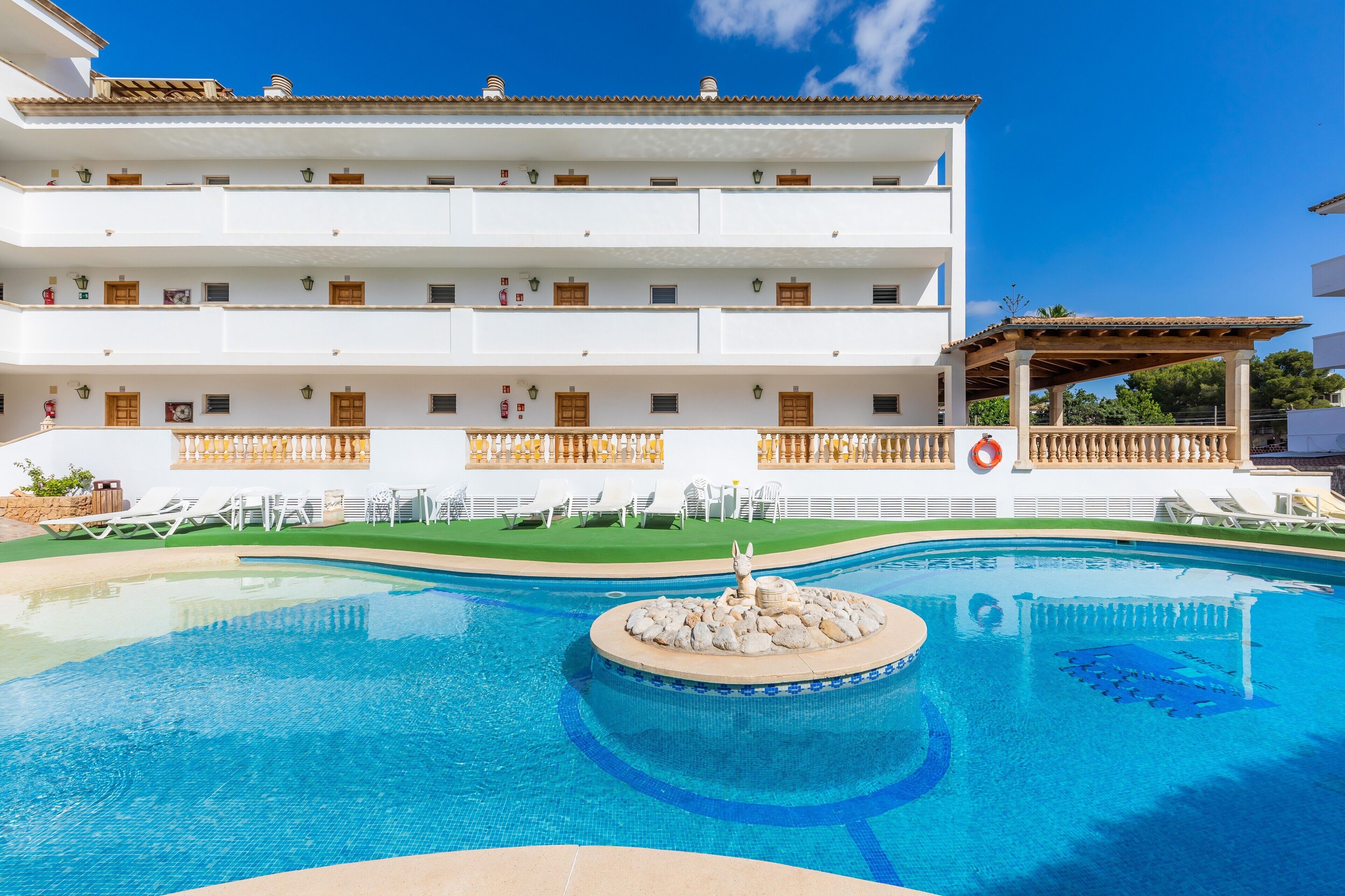 A hotel with a swimming pool, sun loungers, and a covered area.