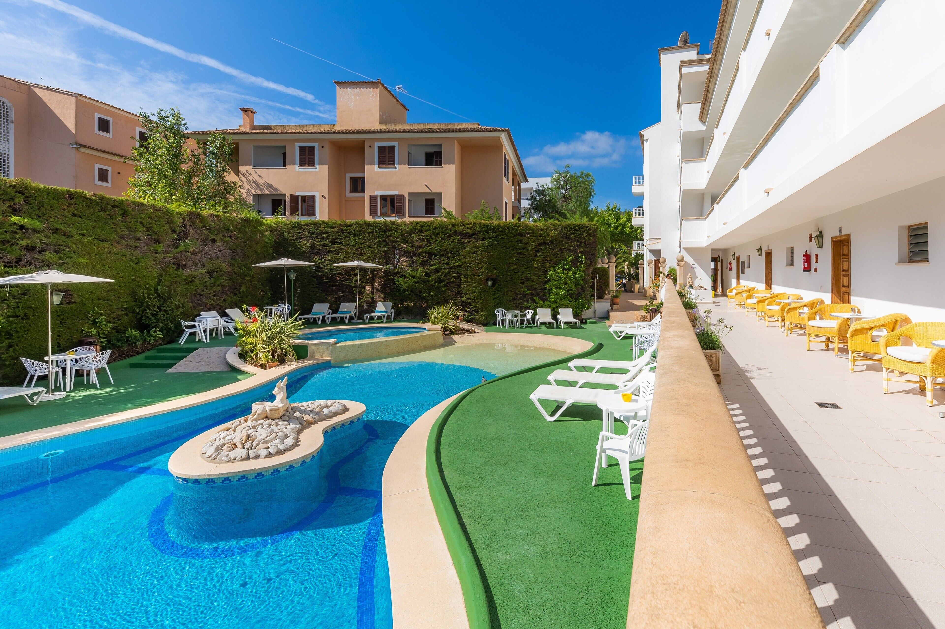 A swimming pool with lounge chairs, a small island, and a building with balconies.