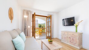 Un salon avec un canapé, une table, un meuble, un téléviseur et une vue sur l’extérieur, visible à travers une porte ouverte.