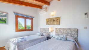 Ein Zimmer mit zwei Betten, einem Fenster, einer Klimaanlage und einem Bild an der Wand.