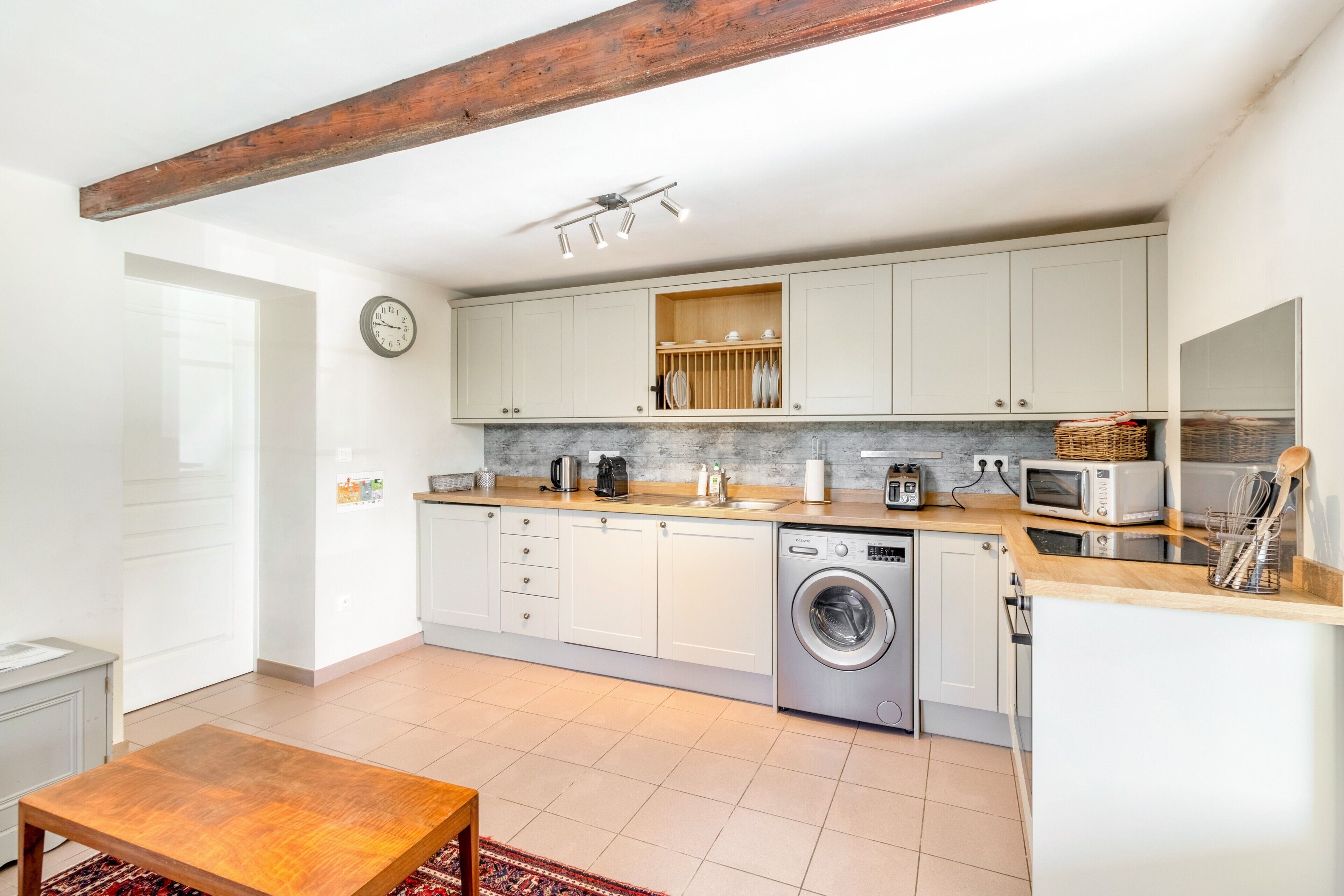 A modern kitchen with white cabinets, a built-in washing machine, and a wooden table.
