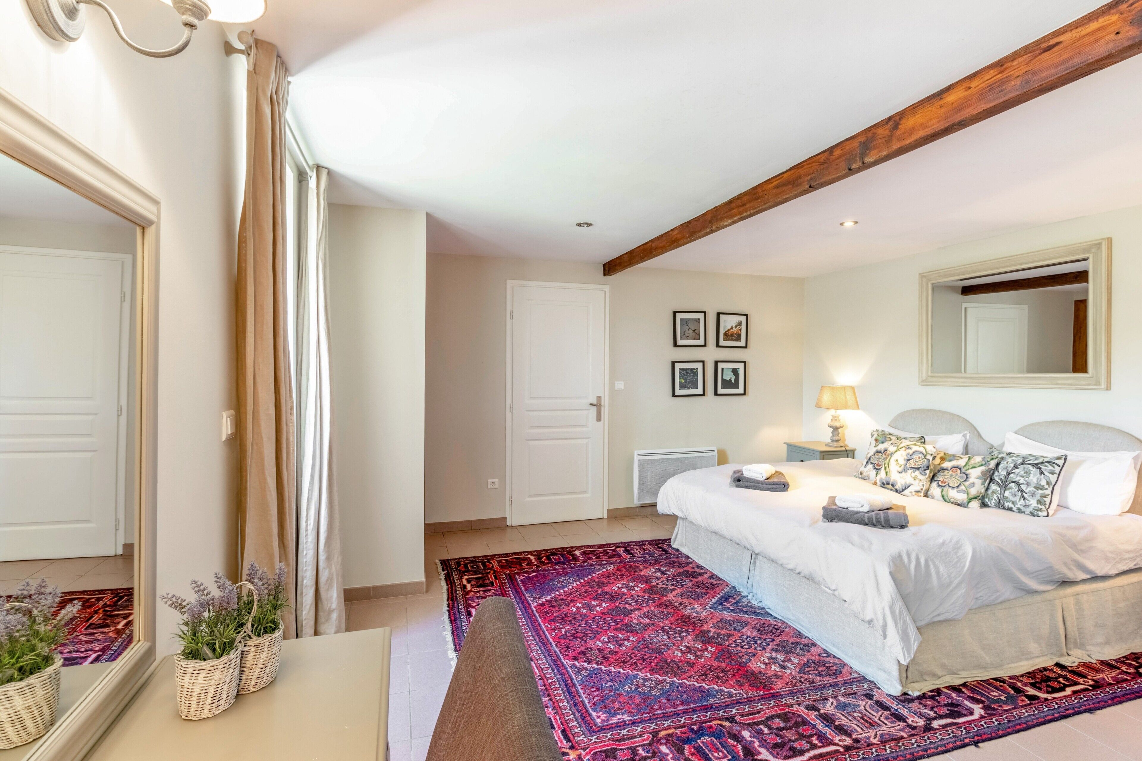 Une chambre à coucher avec un grand lit, un miroir, une table de chevet, une commode, une lampe et un tapis rouge à motifs.