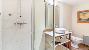 Un bagno con doccia vetrata, un lavandino bianco su mobile in legno e un water.