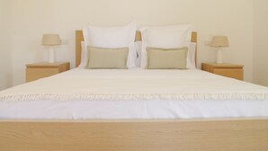 Een opgemaakt bed met een houten hoofdeinde, twee nachtkastjes met lampen, en een effen muur.