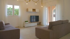 Een moderne woonkamer met een flatscreen televisie, twee banken, een klein wit kastje en een potplant.
