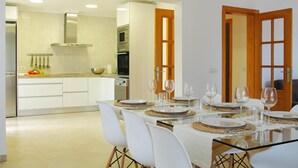 Een moderne keuken met witte kasten, een magnetron en een fornuis. Er is een eethoek met een glazen tafel en witte stoelen.