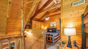 Un dormitorio de cabaña rústica con cama, lámpara y televisor montado en la pared.