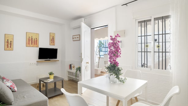 A modern living room with a sofa, a dining table, chairs, a TV, and artwork on the wall.