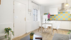 A modern kitchen with white cabinets, a dining area with a table and chairs, and a living area with a sofa.