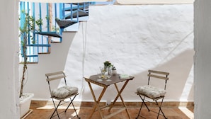 A small patio with a table and two chairs, a potted plant, and a blue railing.