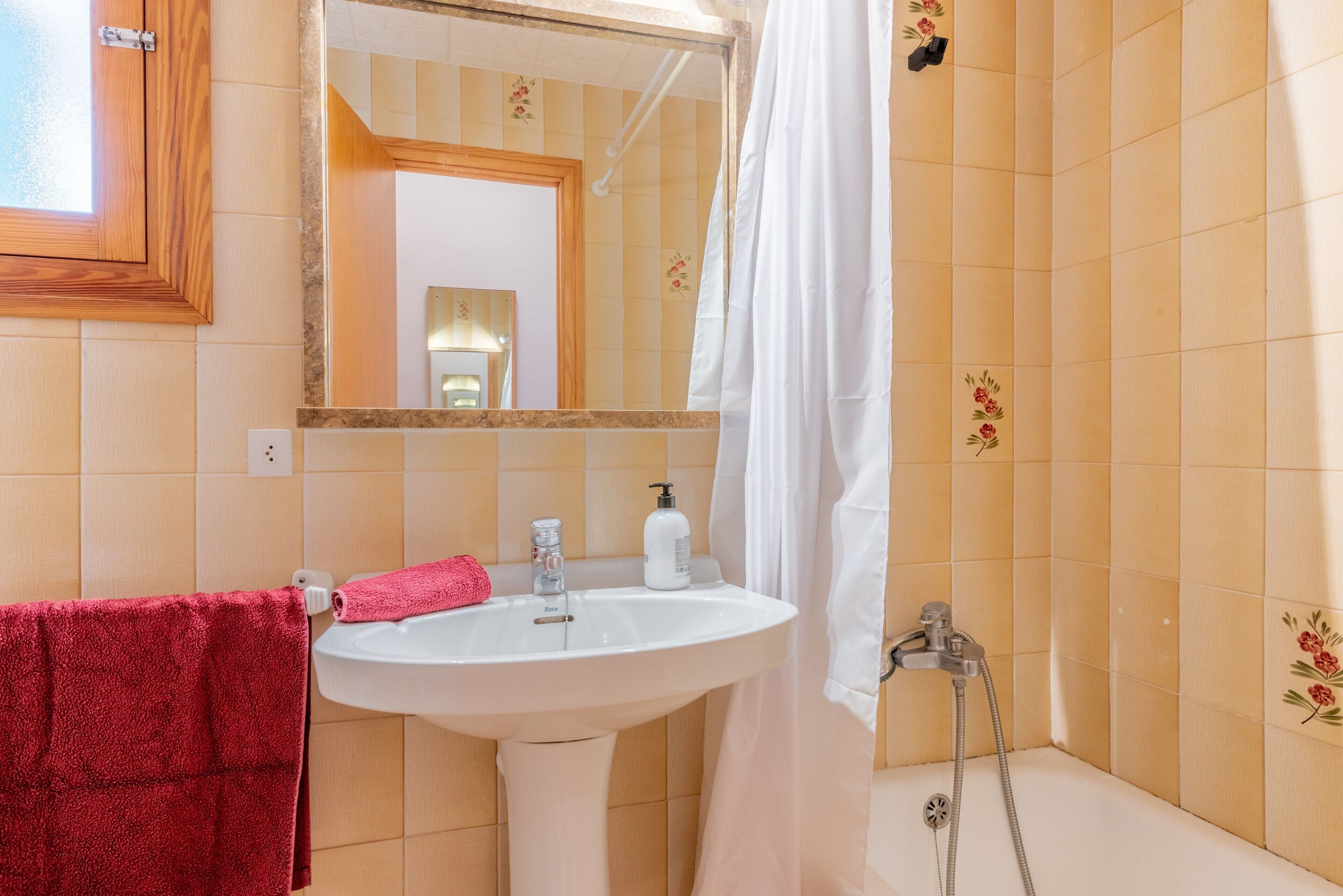 Een badkamer met een wastafel, spiegel, douche en een rode handdoek.