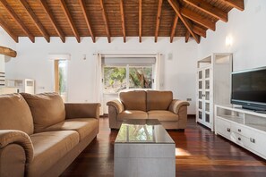 Sala de estar com dois sofás, uma mesa de centro, televisão e teto de madeira.