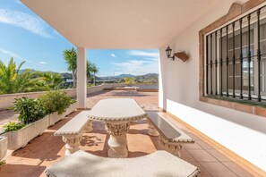 A patio with a stone table and benches, a view of mountains, and a window with a metal grill. - Beautiful Holiday Home “Chalet andaluz Los Alberos” with Mountain View (Coín)