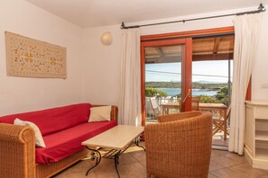 Een balkon met rieten meubels, een rode bank en uitzicht op zee.
