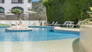 Ein Swimmingpool mit Liegestühlen, einem dekorativen Felsenkörper und einem Gebäude mit Balkonen im Hintergrund.