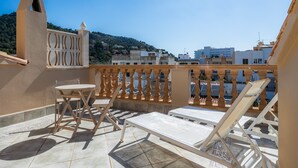 Eine Terrasse mit Tisch und Stühlen, einem Geländer und Blick auf Gebäude und Hügel.
