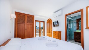 Ein Schlafzimmer mit Bett, Holzschrank, Fernseher und einem Badezimmer mit Glasdusche.