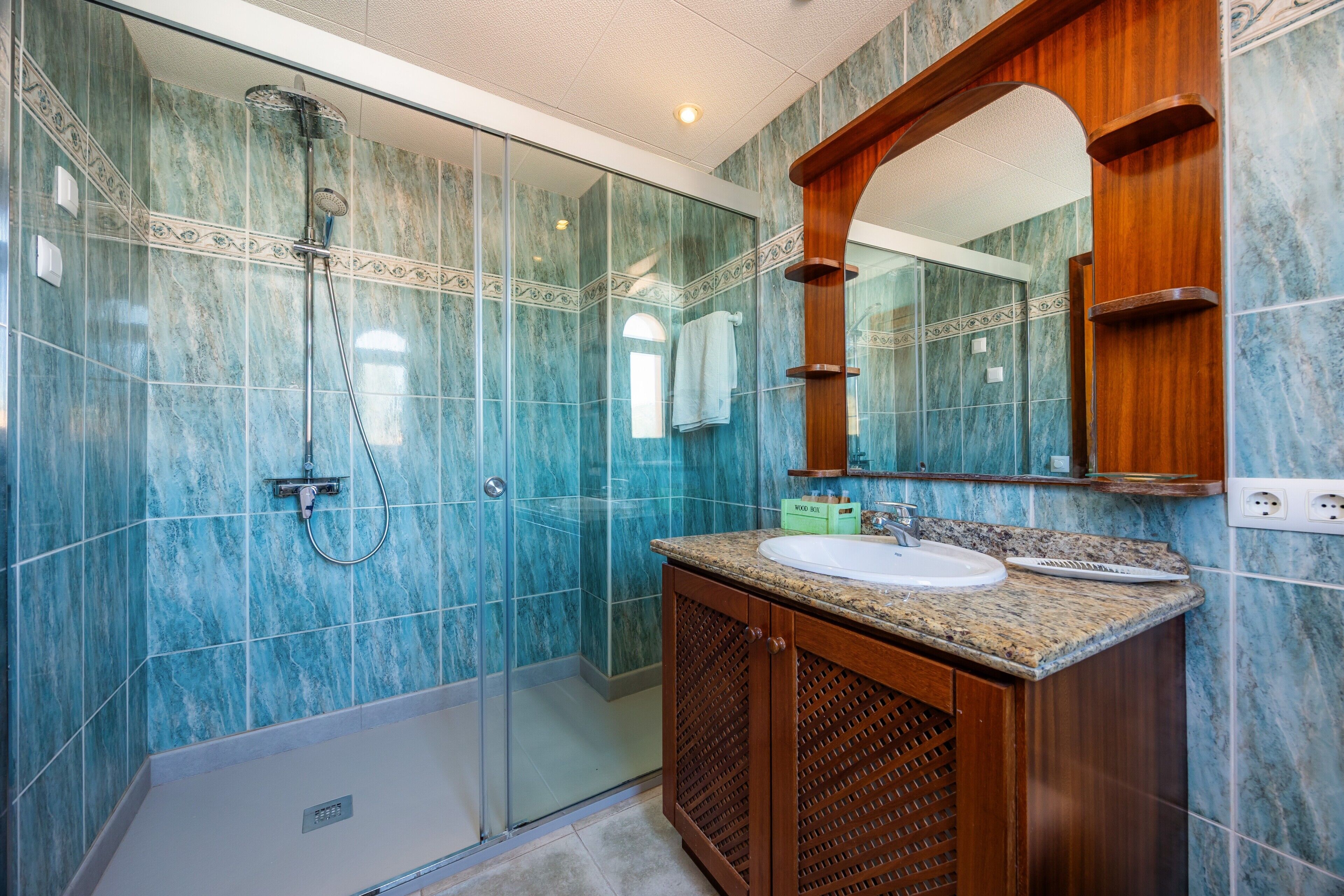 A bathroom with a glass shower enclosure, a wooden vanity with a sink, and a large mirror.