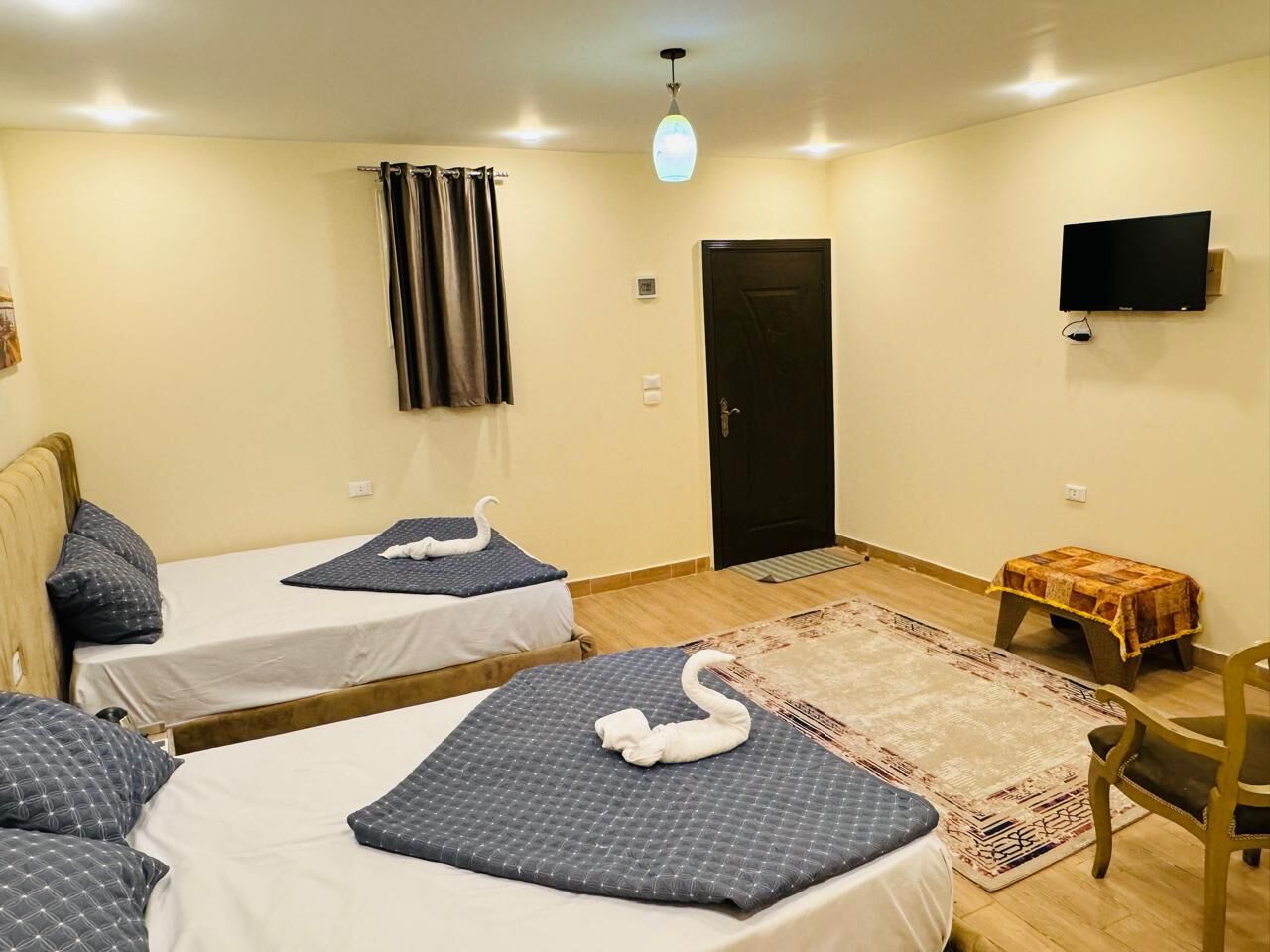 A hotel room with two beds, a flat-screen TV, a small table, and a door.