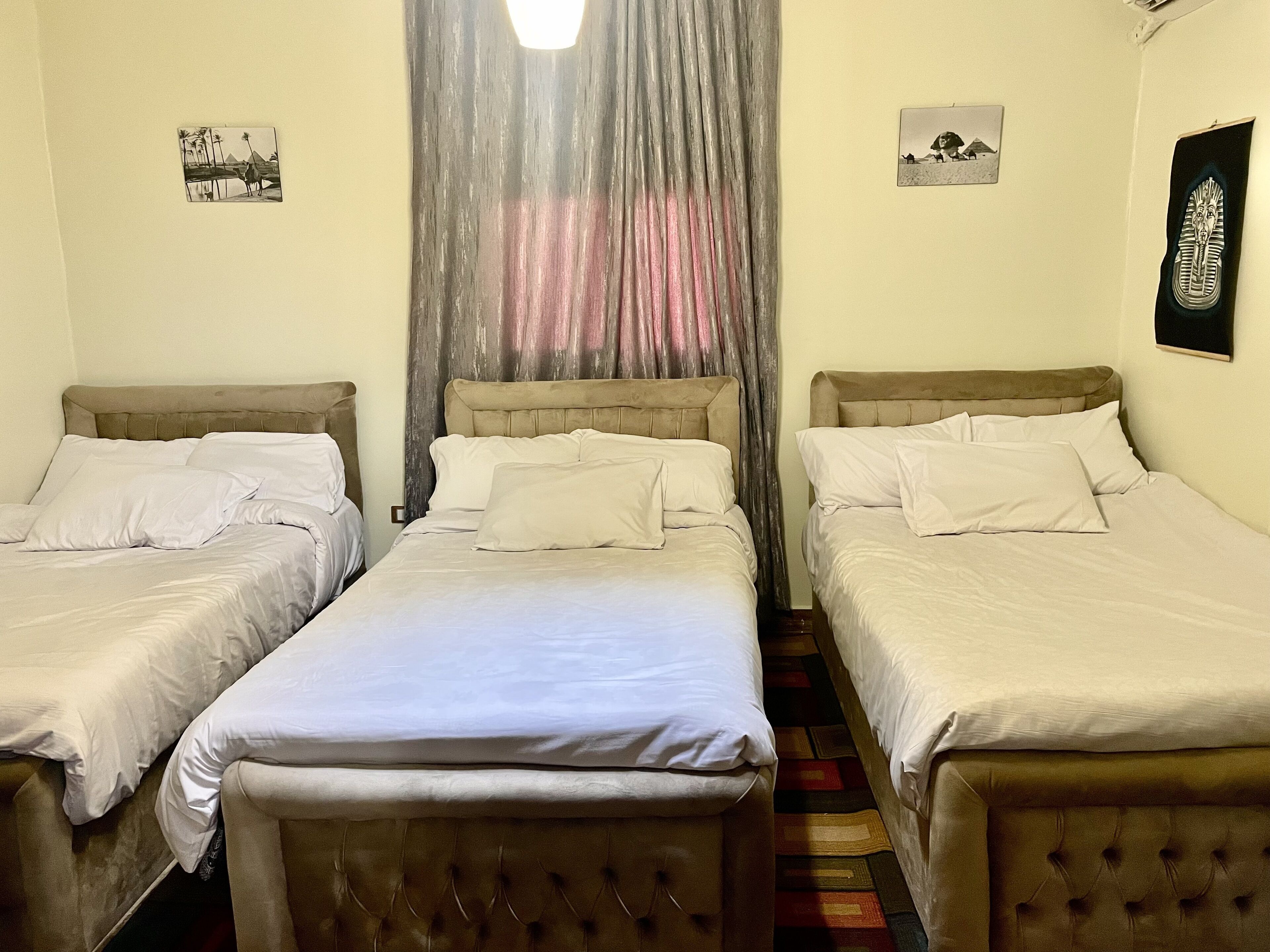 A room with two single beds, a large window with sheer curtains, and a wall-mounted picture of a desert scene.