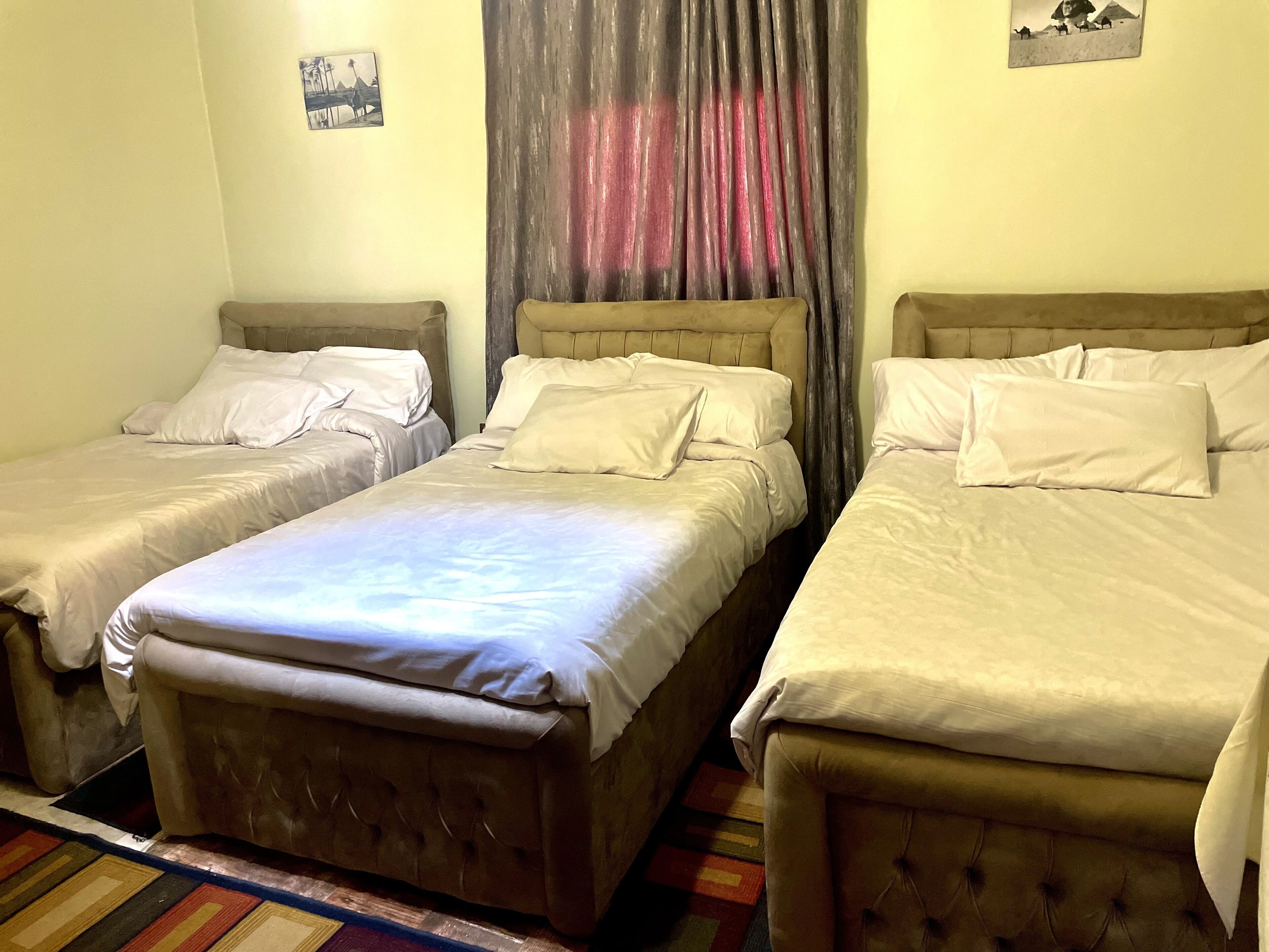 A room with three single beds, a large window with curtains, and a colorful rug.