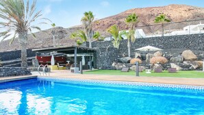 Une piscine bordée d’un mur en pierre, avec des palmiers en arrière-plan.
