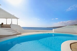 Ein Pool mit Meerblick, ein überdachter Sitzbereich und ein weißes Gebäude.