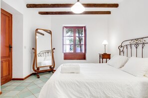 A bedroom with a bed, a wooden wardrobe, a mirror, a window, and a bedside table with a lamp.