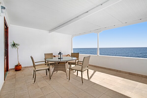 Een terras buiten met een ronde tafel en stoelen, een potplant en uitzicht op zee.