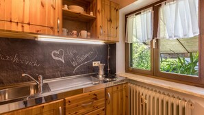 Eine Küche mit Holzausstattung, einer Tafel mit Schrift, einer Edelstahlspüle und einem Fenster mit Vorhängen.
