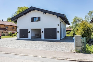 A two-story building with a garage, cobblestone driveway, and a green fence.