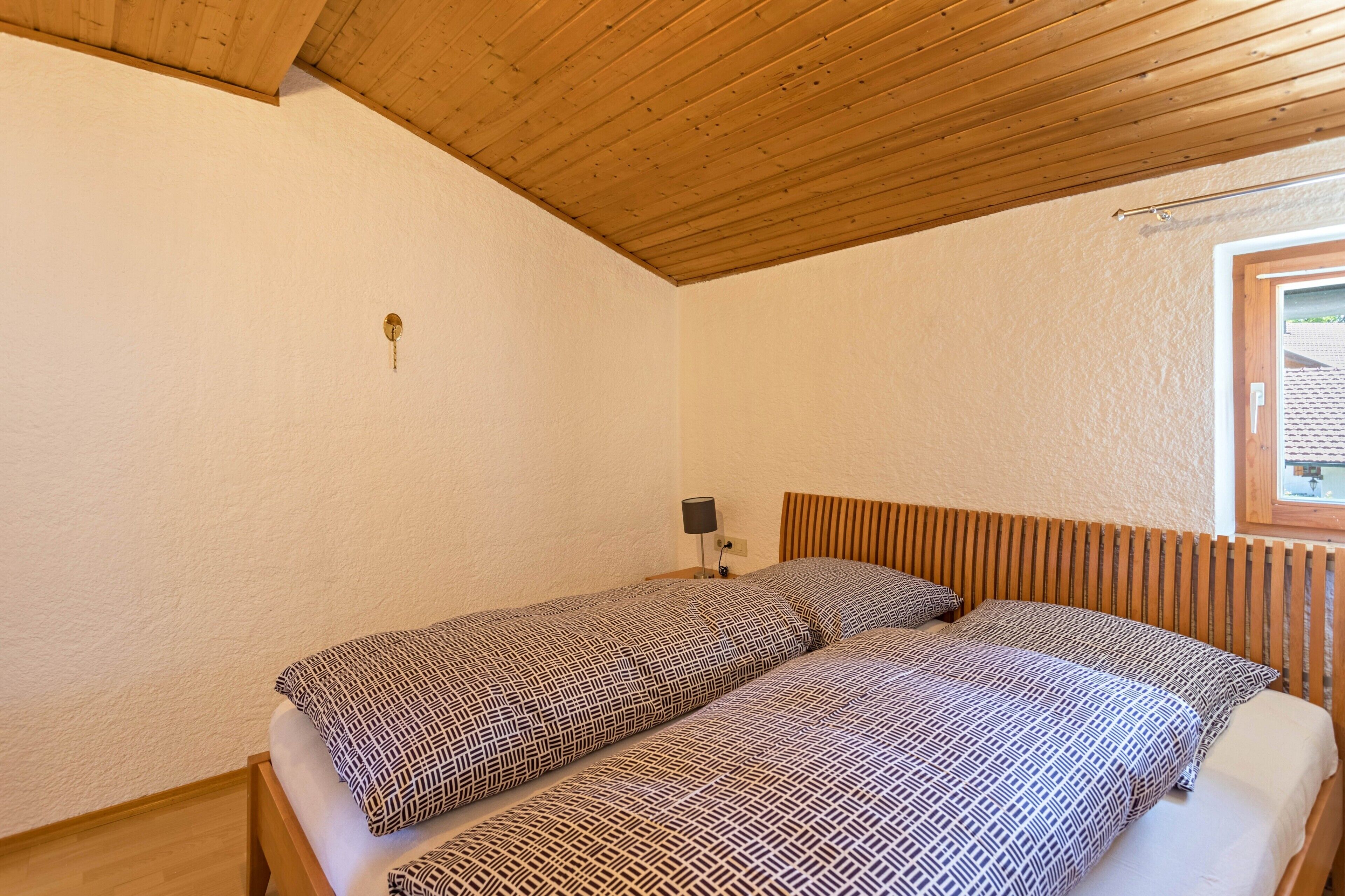 Un dormitorio con dos camas, techo de madera, una mesita de noche con lámpara y ventana con vistas.