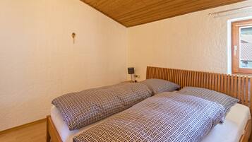 Un dormitorio con dos camas, techo de madera, una mesita de noche con lámpara y ventana con vistas.