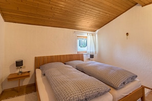 A bedroom with a wooden ceiling, a bed with patterned bedding, a nightstand with a lamp, and a window with curtains.