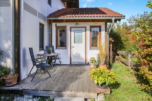 Un patio in legno con tavolo e sedie, un edificio bianco con tetto in tegole rosse e piante in vaso.